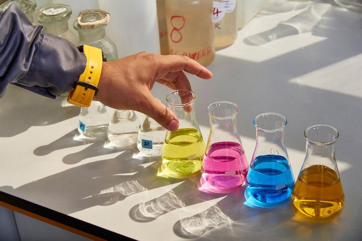 worker's hand in lab setting with fluid-filled beakers in various colors worker's hand in lab setting with fluid-filled beakers in various colors