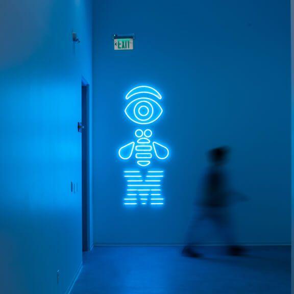 neon rebus in hallway with person walking nearby neon rebus in hallway with person walking nearby